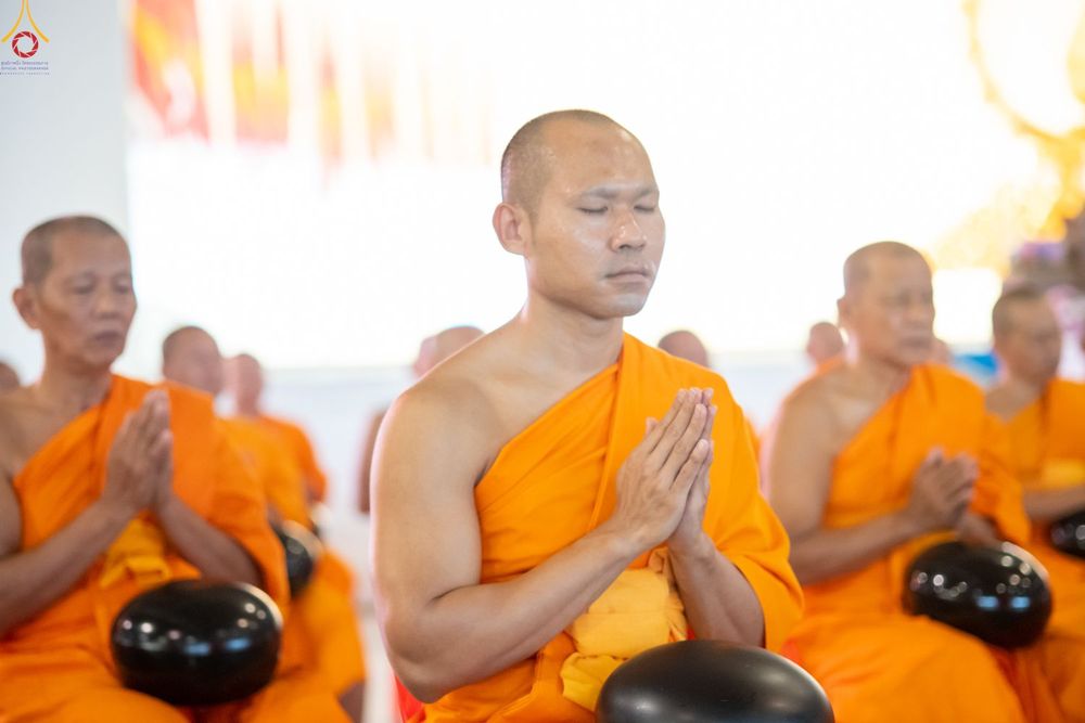 พระภิกษุสงฆ์หลายรูปกำลังนั่งพนมมือหลับตาทำสมาธิในพิธีทางศาสนา