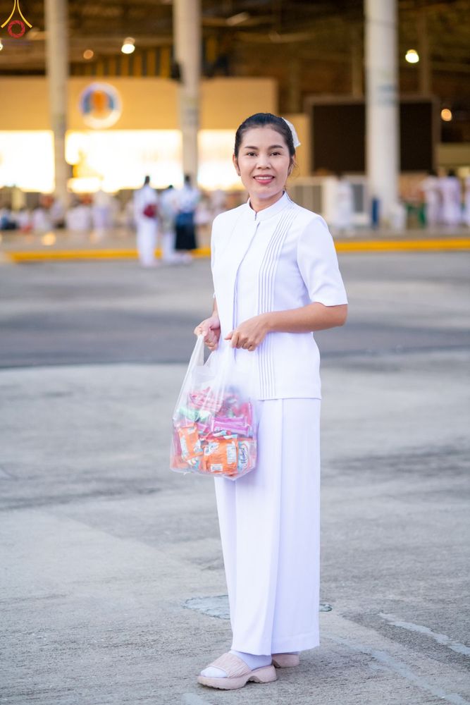 หญิงสาวสวมชุดสีขาวถือถุงอาหารแห้งยืนยิ้มให้กล้องในพื้นที่อาคารกว้างขวาง