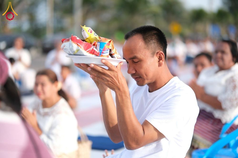 ชายไทยสวมเสื้อสีขาวถือจานอาหารแห้งเพื่อเตรียมตักบาตรพระในพิธีทำบุญ