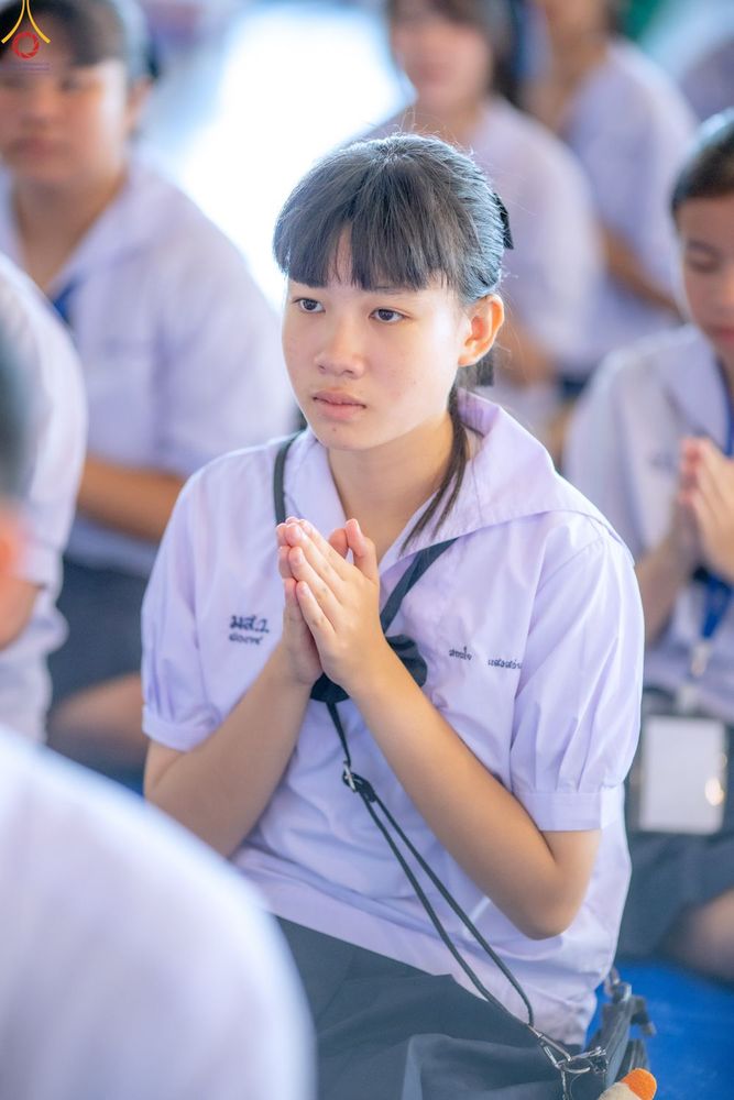 นักเรียนหญิงสวมชุดนักเรียนสีขาวกำลังนั่งพนมมือไหว้ด้วยความตั้งใจในพิธีทางศาสนา