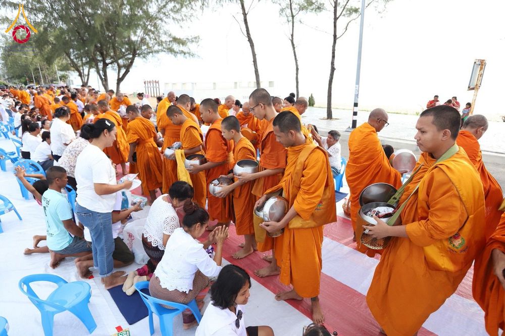 พระสงฆ์ในจีวรสีส้มกำลังเดินรับบิณฑบาตจากประชาชนที่นั่งรอใส่บาตรอยู่ริมชายหาด