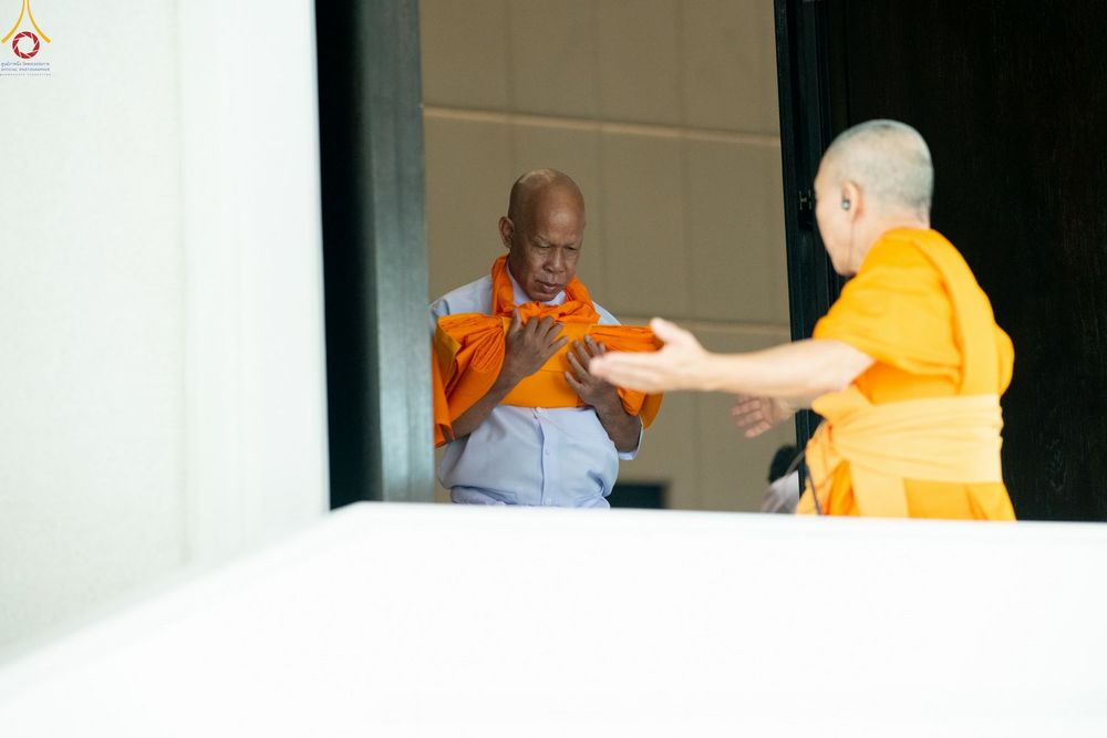 พระภิกษุสงฆ์กำลังให้คำแนะนำแก่ผู้เข้าร่วมโครงการอุปสมบทที่ถือผ้าไตรจีวรในมือ