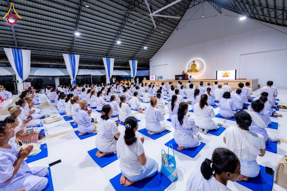 กลุ่มคนสวมชุดขาวนั่งปฏิบัติธรรมบนเบาะสีน้ำเงินภายในอาคาร