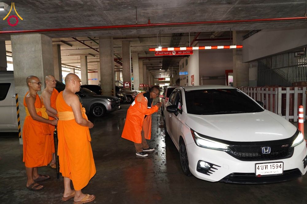เจ้าอาวาสวัดพระธรรมกายและคณะสงฆ์ยืนดูเจ้าหน้าที่ทำความเคารพรถยนต์สีขาวภายในอาคารจอดรถ