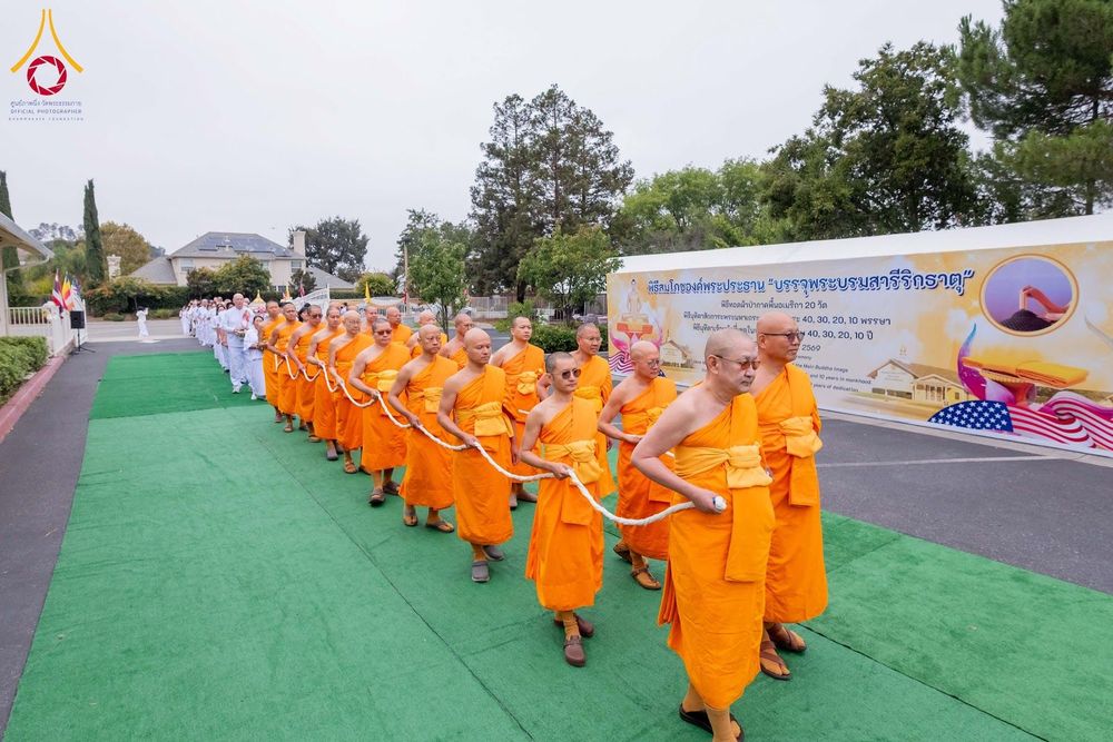 คณะสงฆ์ถือสายสิญจน์เดินแถวในพิธีทางศาสนาท่ามกลางบรรยากาศกลางแจ้ง
