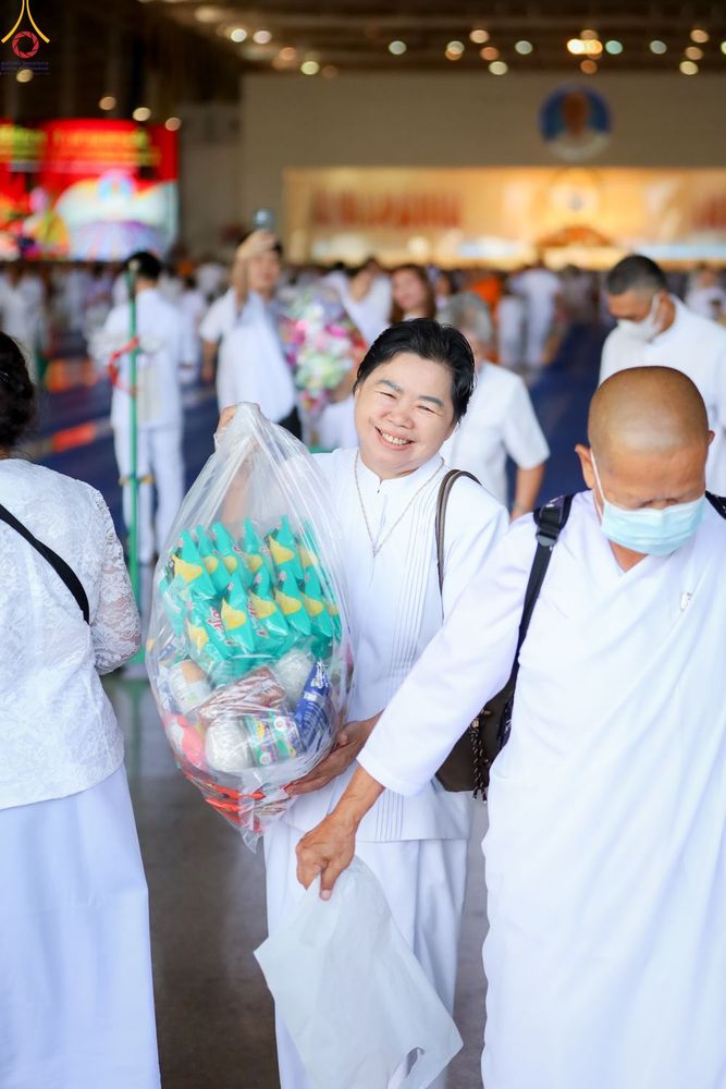 หญิงไทยสวมชุดขาวถือถุงใส่ของตักบาตรด้วยรอยยิ้มในพิธีทำบุญ
