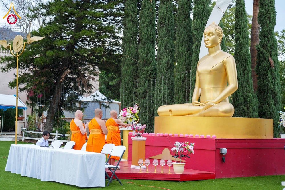 พระภิกษุ 3 รูปกำลังประกอบพิธีกรรมหน้าพระพุทธรูปสีทองขนาดใหญ่กลางแจ้ง