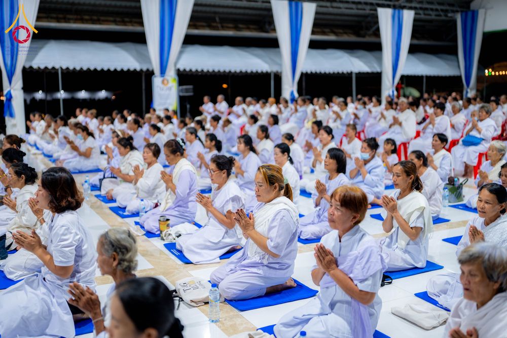 กลุ่มคนสวมชุดสีขาวนั่งพนมมือปฏิบัติธรรมในอาคาร