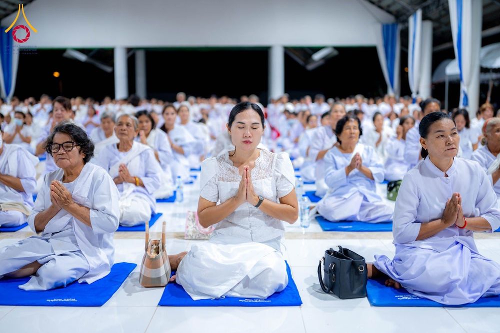 กลุ่มอุบาสิกาสวมชุดสีขาวนั่งพนมมือหลับตาปฏิบัติธรรมภายในอาคาร
