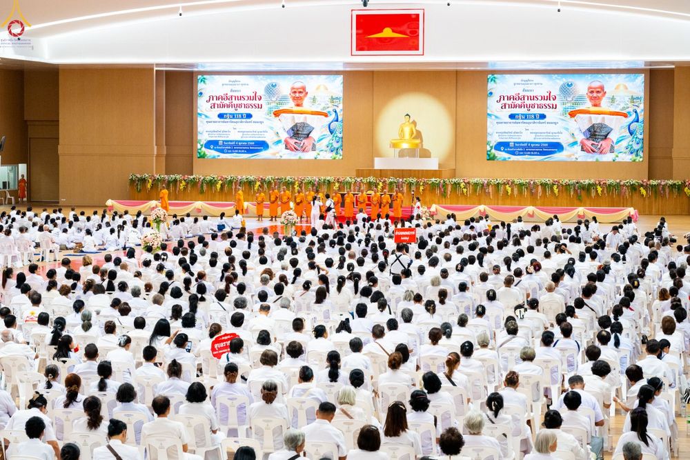 ผู้คนจำนวนมากสวมชุดสีขาวนั่งฟังบรรยายในหอประชุมขนาดใหญ่ที่มีพระภิกษุสงฆ์อยู่บนเวที