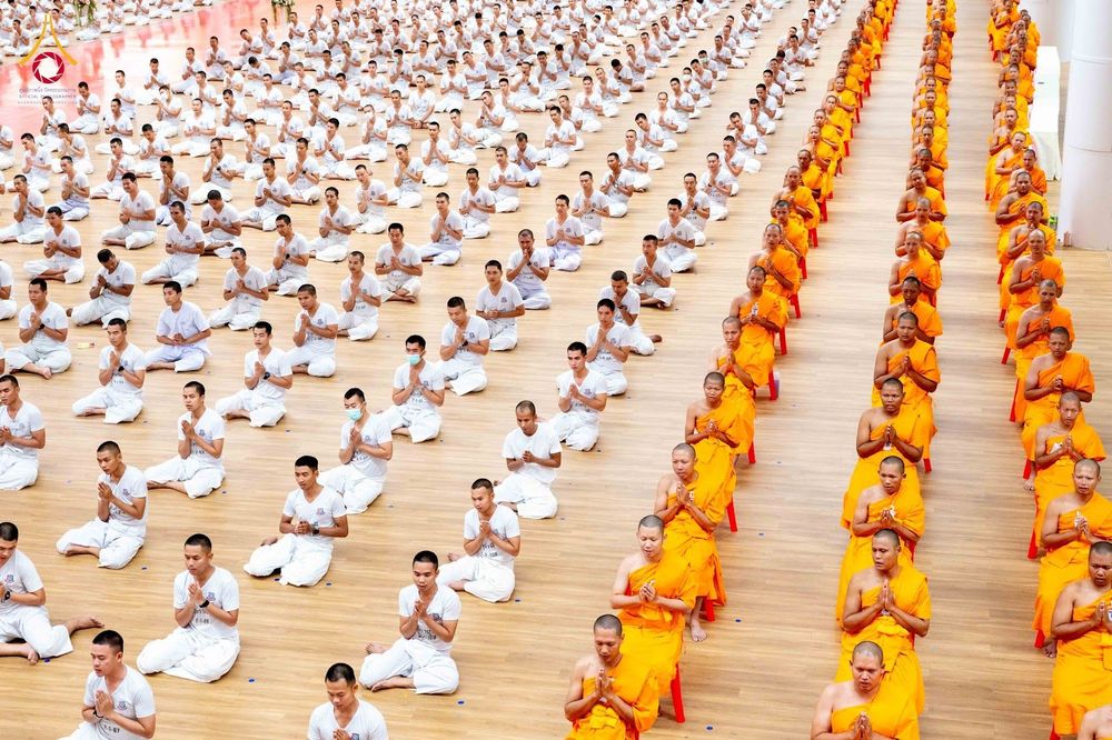กลุ่มนักเรียนนายสิบตำรวจในชุดผ้าไตรจีวรสีเหลืองนั่งพนมมือเรียงแถวอย่างเป็นระเบียบภายในอาคาร