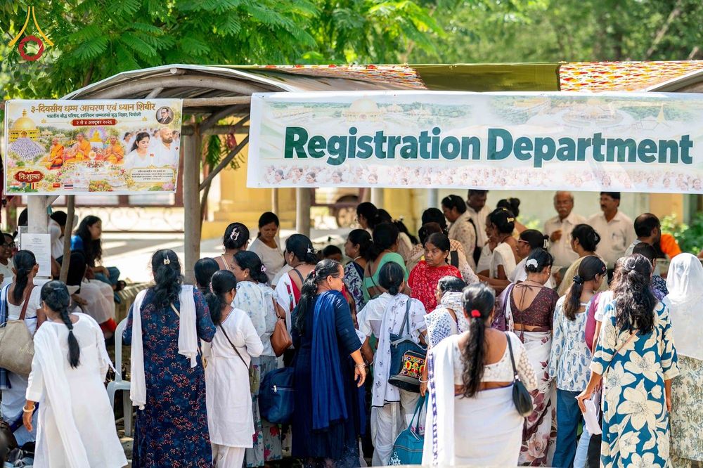 ผู้คนจำนวนมากกำลังยืนรอที่จุดลงทะเบียนที่มีป้ายข้อความ Registration Department ในสถานที่กลางแจ้ง