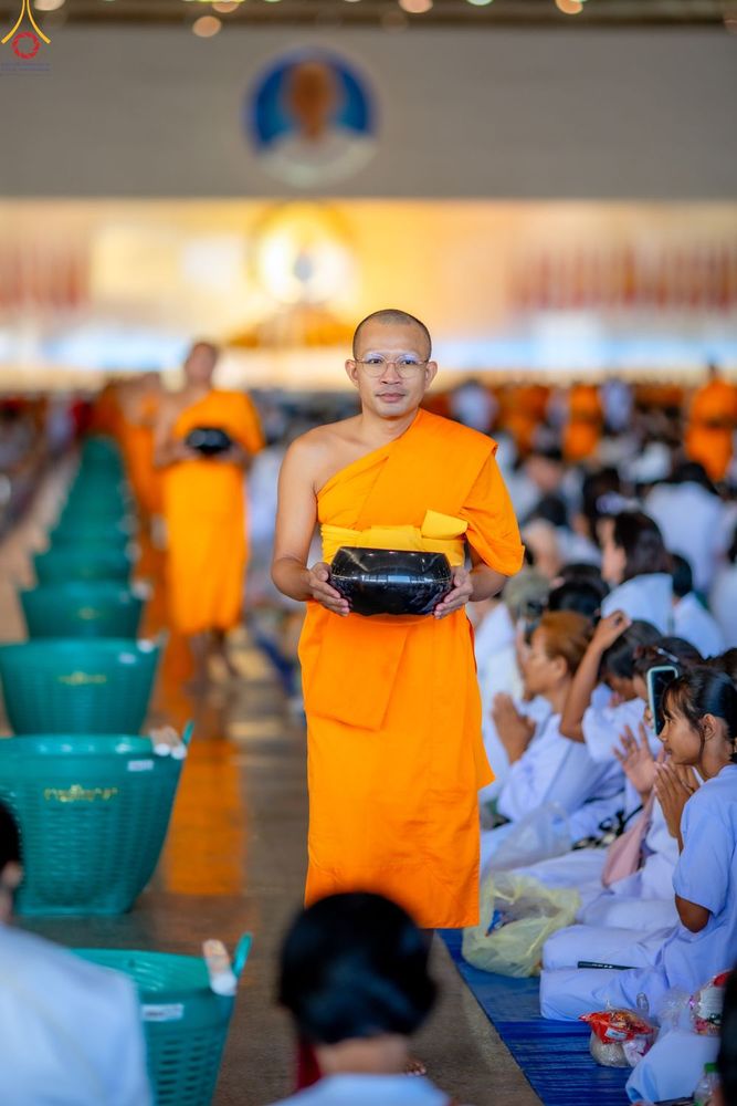 พระภิกษุสงฆ์ถือบาตรเดินรับบิณฑบาตท่ามกลางพุทธศาสนิกชนที่นั่งพนมมือรอใส่บาตรในอาคาร
