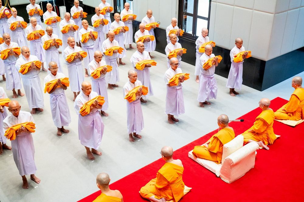 กลุ่มนาคชายในชุดขาวถือผ้าไตรยืนรอประกอบพิธีบรรพชาอุปสมบทต่อหน้าพระภิกษุสงฆ์ภายในอาคาร