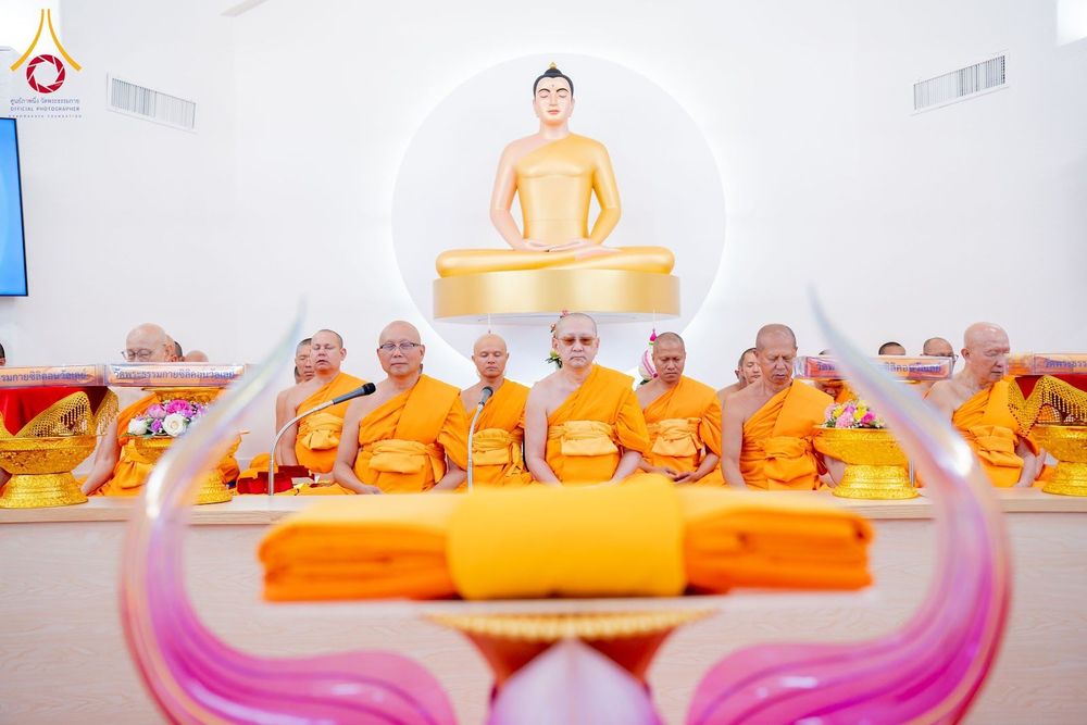 คณะสงฆ์ห่มจีวรสีเหลืองนั่งเรียงแถวหน้าพระพุทธรูปสีทองในพิธีทางศาสนา