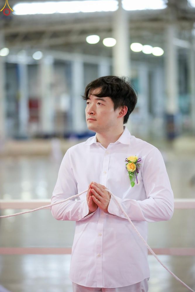 ชายหนุ่มสวมเสื้อสีขาวประนมมือถือสายสิญจน์ในพิธีกรรม