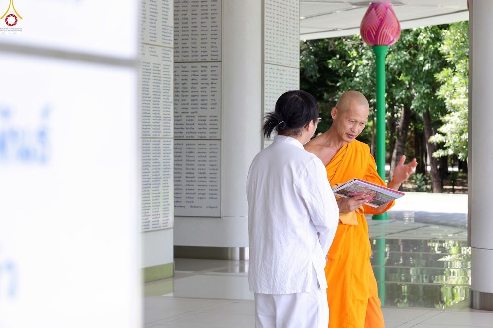 พระภิกษุสนทนากับผู้มาเยือนในชุดสีขาวขณะถือเอกสารประกอบการอธิบาย