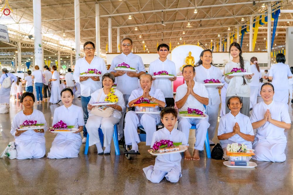กลุ่มพุทธศาสนิกชนสวมชุดขาวถือถาดดอกไม้และของตักบาตรภายในอาคารสภาธรรมกายสากล