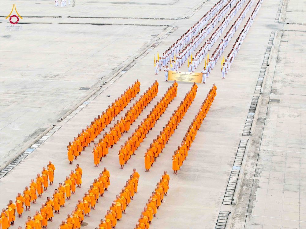 แถวพระภิกษุในจีวรสีส้มและกลุ่มคนในชุดสีขาวเดินเรียงแถวอย่างเป็นระเบียบในลานกว้าง