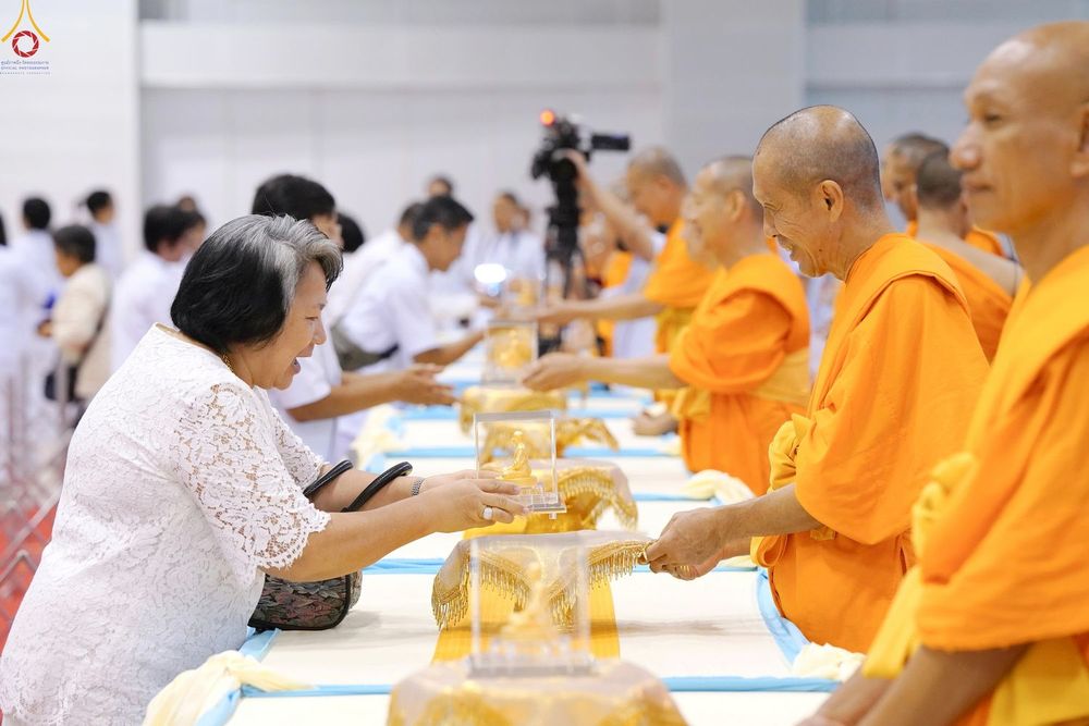 หญิงวัยกลางคนสวมชุดสีขาวกำลังรับพระของขวัญจากพระภิกษุสงฆ์ในพิธีมอบพระของขวัญ