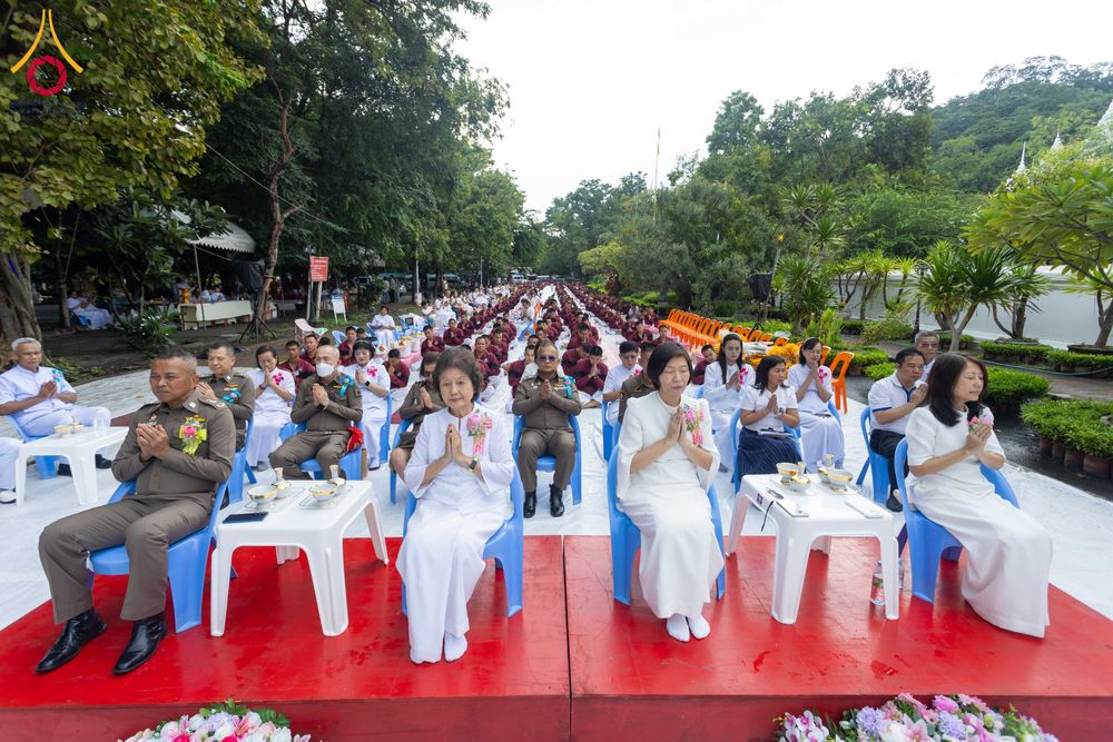 กลุ่มข้าราชการตำรวจและประชาชนในชุดสีขาวนั่งพนมมือร่วมพิธีตักบาตรสามเณรกลางแจ้ง