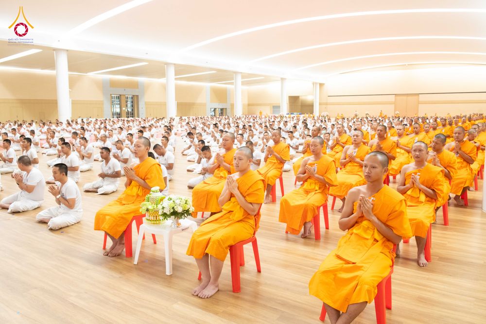 กลุ่มผู้เข้าร่วมโครงการบรรพชาในชุดจีวรสีเหลืองนั่งพนมมือเรียงแถวภายในหอประชุม