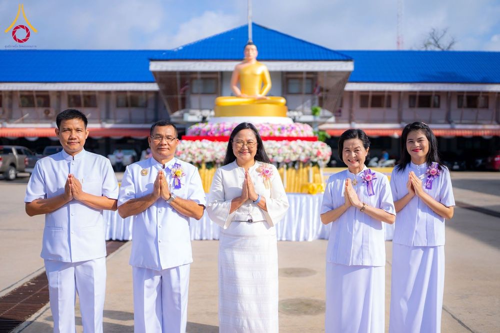 กลุ่มบุคคลชายหญิงสวมชุดสีขาวพนมมือไหว้ ด้านหลังเป็นพระพุทธรูปและอาคาร