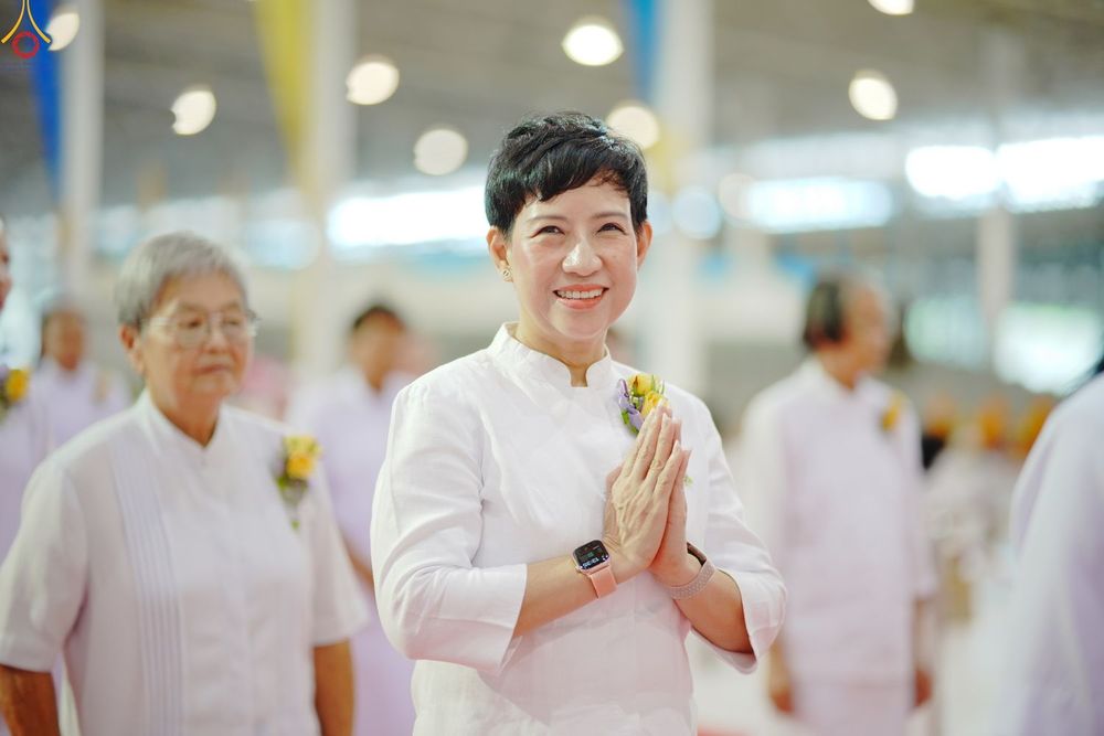 หญิงไทยผมสั้นสวมชุดสีขาวกำลังพนมมือไหว้ด้วยรอยยิ้มในงานพิธี