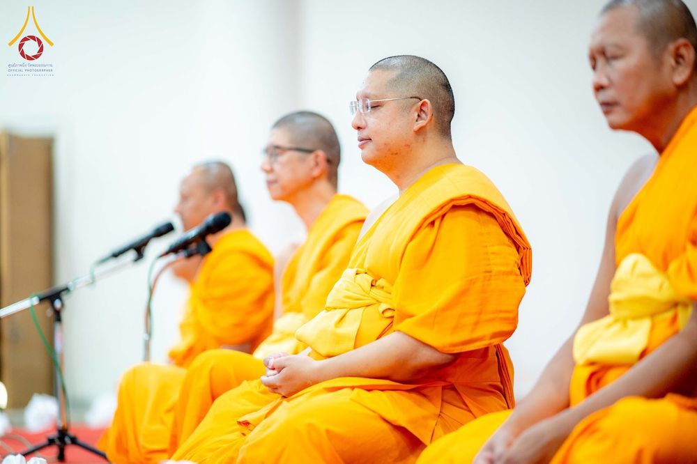 พระสงฆ์หลายรูปนั่งสมาธิเรียงแถวในพิธีทางศาสนาโดยมีไมโครโฟนตั้งอยู่ด้านหน้า