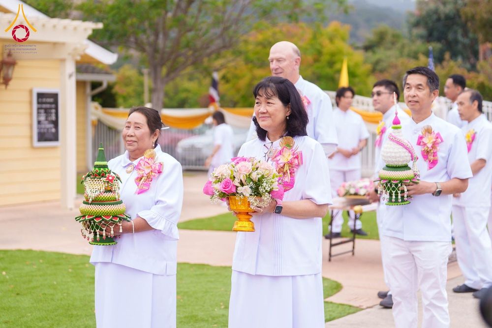 กลุ่มคนสวมชุดขาวถือพานพุ่มและพานดอกไม้เดินในขบวนพิธีทางศาสนา