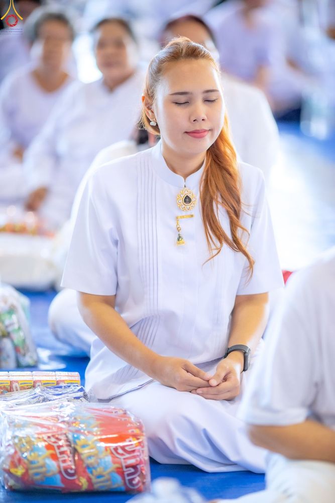 หญิงสาวสวมชุดสีขาวนั่งหลับตาทำสมาธิในพิธีทำบุญตักบาตร