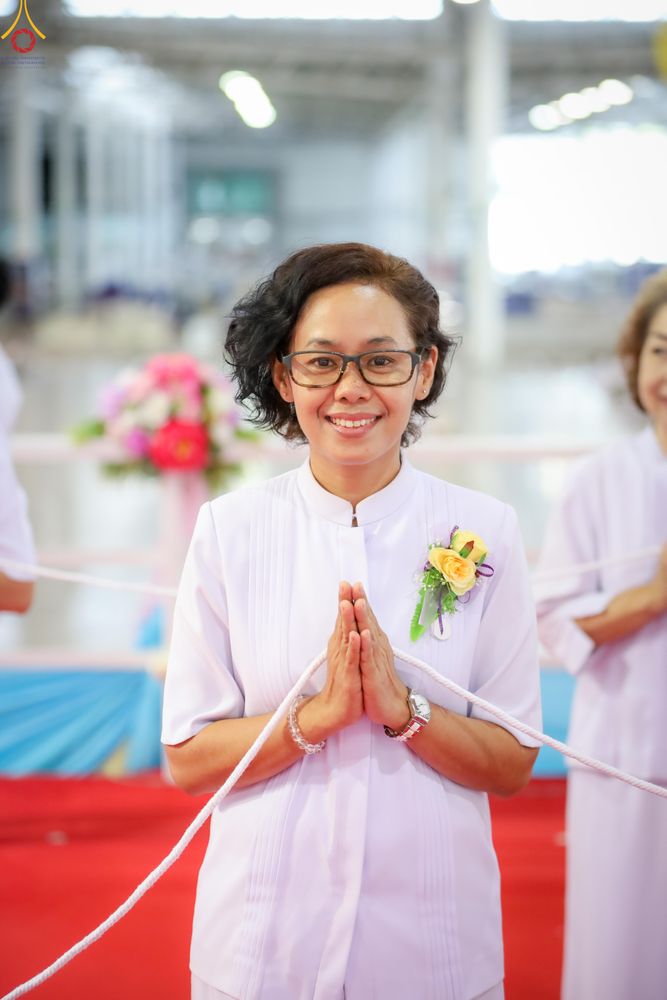 หญิงไทยสวมชุดขาวพนมมือยิ้มแย้มในงานพิธี