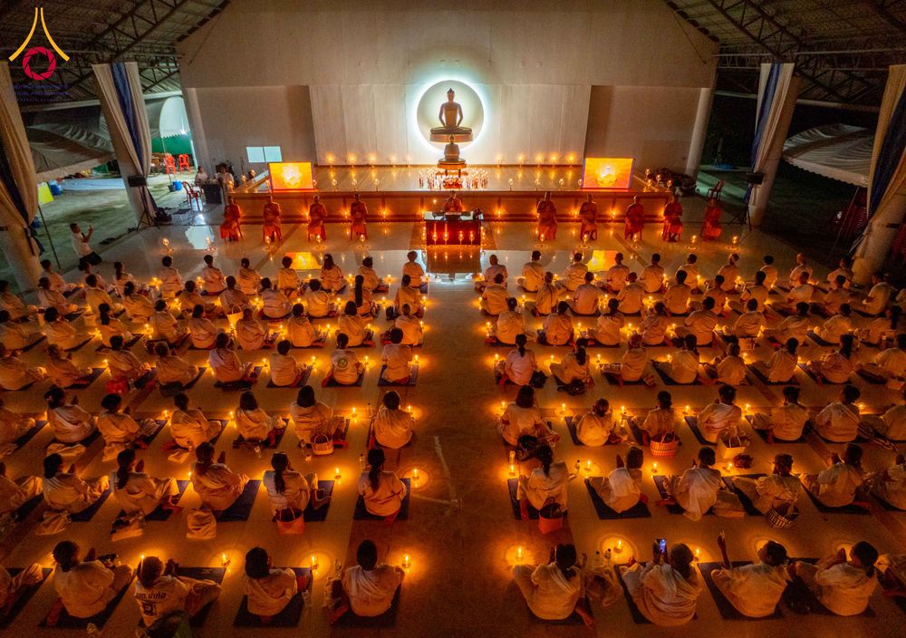 กลุ่มคนสวมชุดขาวนั่งสมาธิท่ามกลางแสงเทียนในอาคารปฏิบัติธรรมที่มีพระพุทธรูปเป็นประธาน