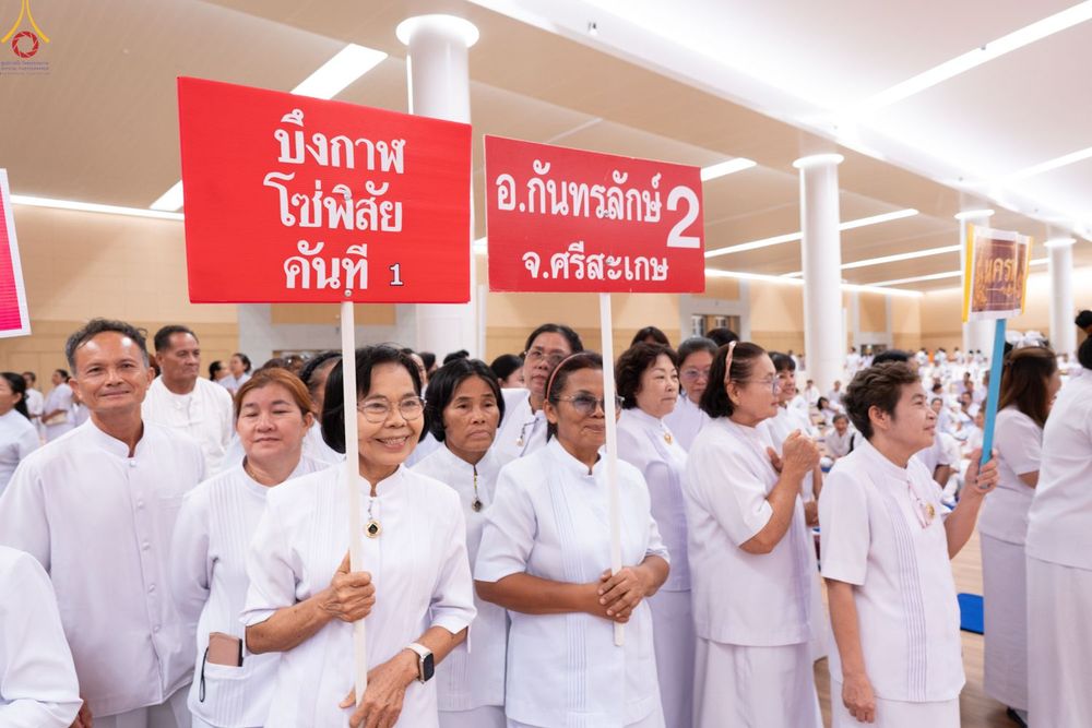 กลุ่มคนสวมชุดสีขาวถือป้ายชื่อจังหวัดและอำเภอในงานสัมมนา