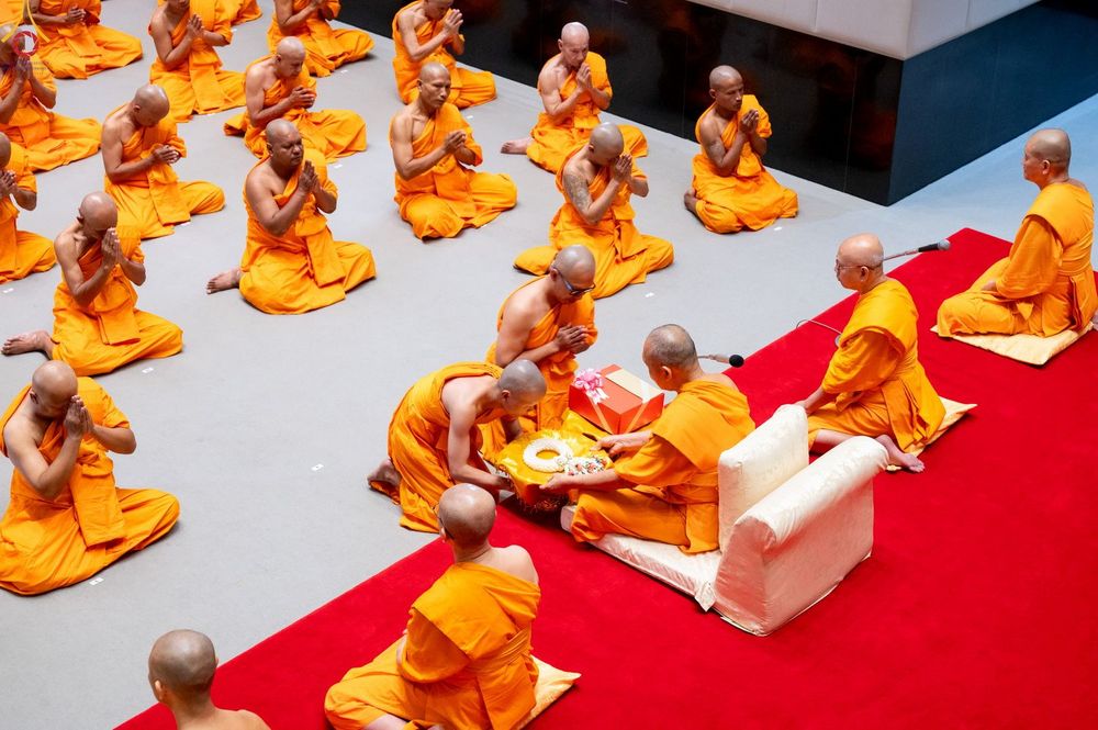 กลุ่มพระภิกษุและนาคในชุดจีวรสีเหลืองทองกำลังประกอบพิธีบรรพชาอุปสมบทภายในโบสถ์