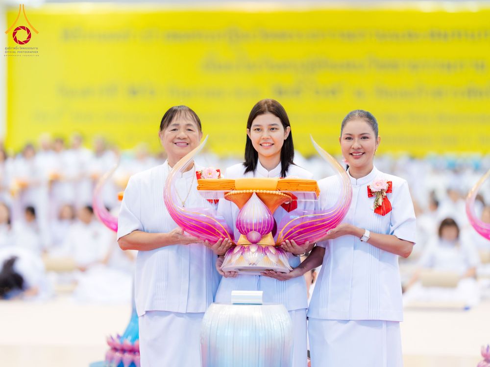 หญิงสามคนในชุดขาวถือพานพุ่มดอกบัวประดับผ้าไตรจีวรในพิธีทางศาสนา