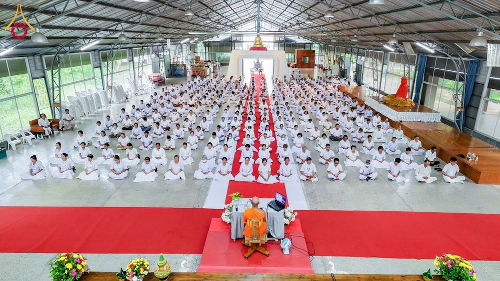 กลุ่มผู้เข้าร่วมโครงการสวมชุดสีขาวนั่งปฏิบัติธรรมภายในอาคารโดยมีพระภิกษุนำสวดมนต์