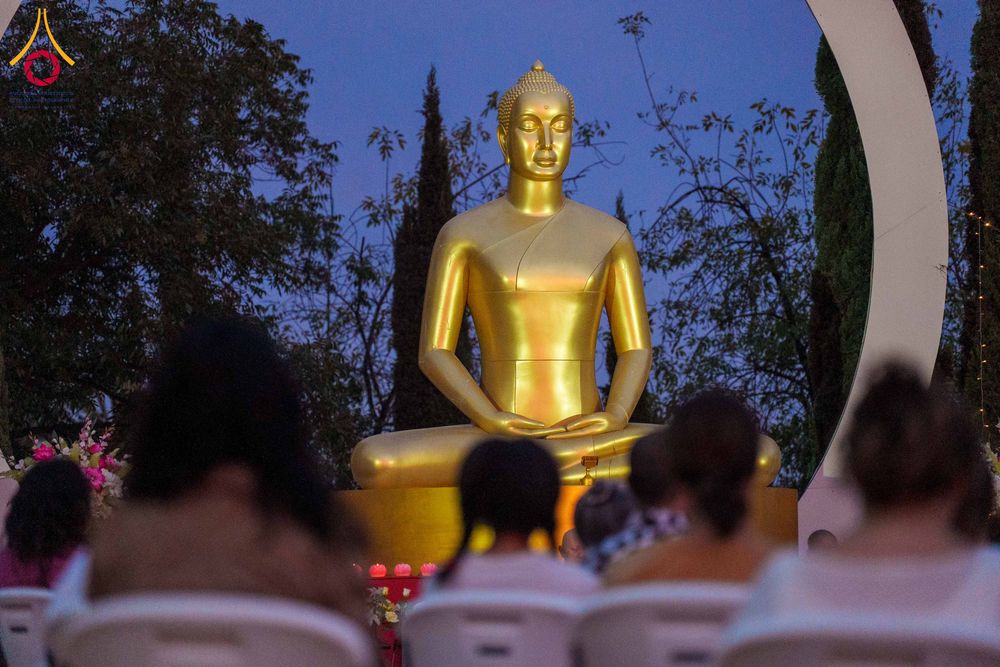 ผู้คนนั่งสมาธิเบื้องหน้าพระพุทธรูปสีทองขนาดใหญ่ในยามค่ำคืน