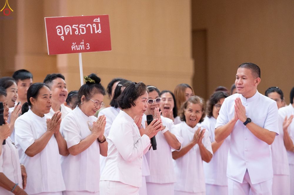 กลุ่มคนสวมชุดสีขาวพนมมือไหว้ในงานสัมมนา โดยมีป้ายข้อความอุดรธานี คันที่ 3 อยู่ด้านหลัง