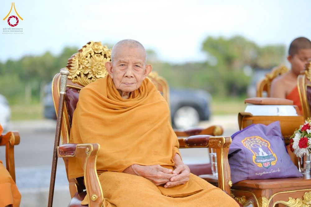 พระภิกษุสงฆ์นั่งบนเก้าอี้ไม้แกะสลักในพิธีตักบาตร