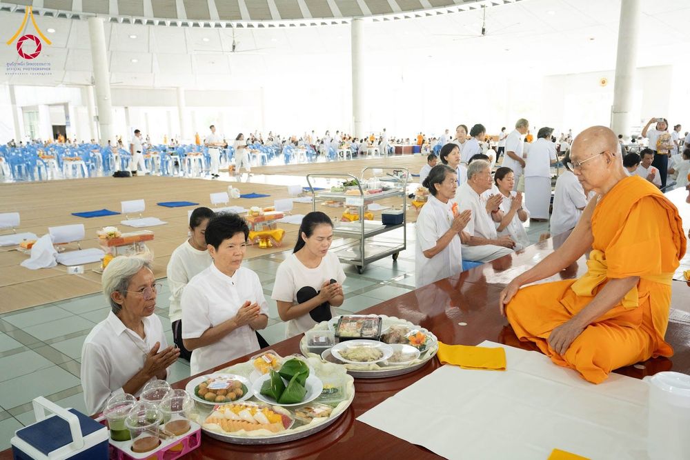 พุทธศาสนิกชนชุดขาวนั่งพนมมือถวายภัตตาหารแด่พระภิกษุสงฆ์ภายในอาคารหอฉัน
