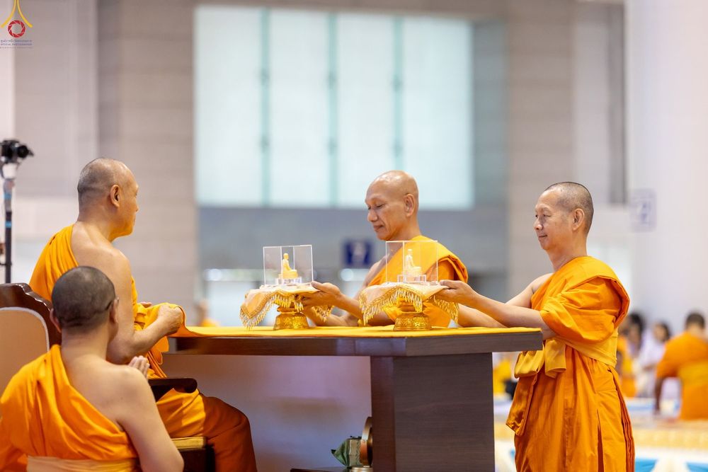 พระภิกษุสงฆ์กำลังประกอบพิธีมอบพระของขวัญในครอบแก้วบนพานทองภายในอาคาร