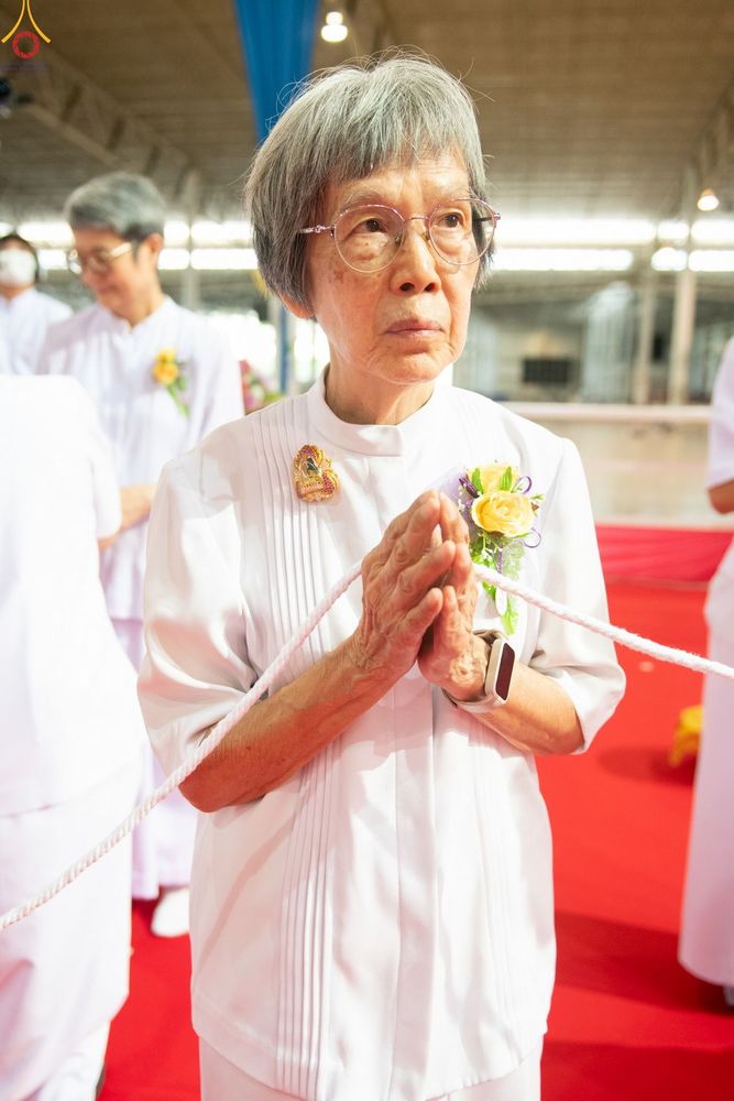 หญิงสูงวัยผมสีเทาสวมชุดสีขาวพนมมืออย่างสงบในพิธีกรรม