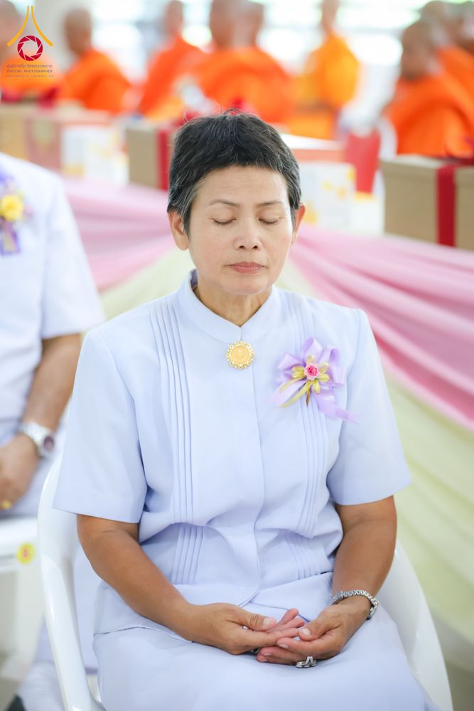 หญิงวัยกลางคนสวมชุดสีขาวนั่งหลับตาทำสมาธิในพิธีทางศาสนา
