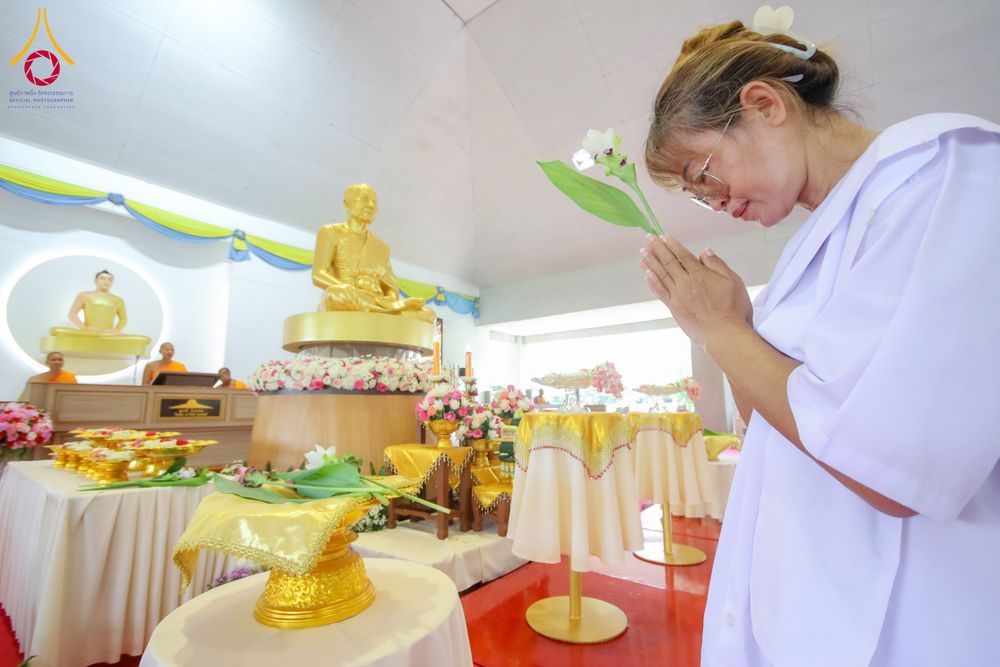 หญิงสวมชุดขาวพนมมือถือดอกไม้กราบไหว้พระพุทธรูปภายในสถานที่ปฏิบัติธรรม