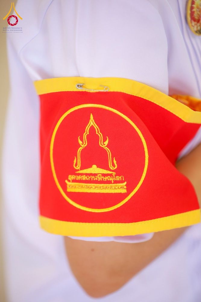 ปลอกแขนสีแดงขอบเหลืองที่มีตราสัญลักษณ์และข้อความธุดงคสถานพิษณุโลกปักอยู่บนผ้า