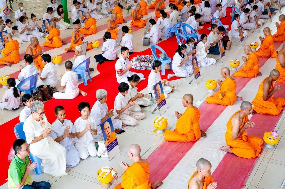 กลุ่มพุทธศาสนิกชนและพระภิกษุสงฆ์นั่งพนมมือร่วมพิธีบรรพชาอุปสมบทภายในอาคาร