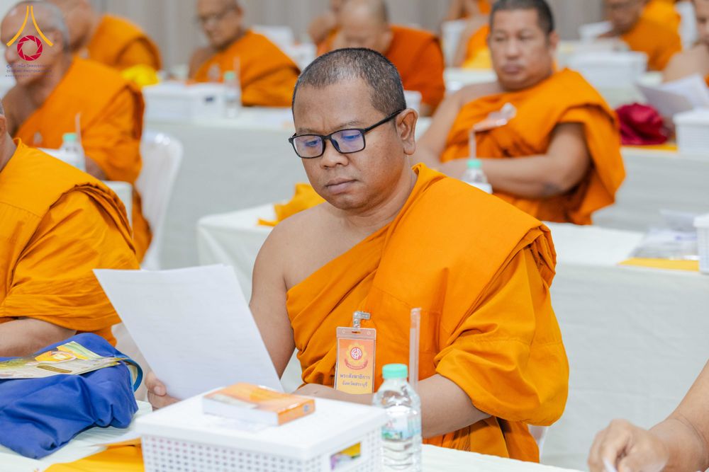 พระภิกษุสงฆ์สวมจีวรสีส้มสวมแว่นตากำลังอ่านเอกสารในห้องประชุม