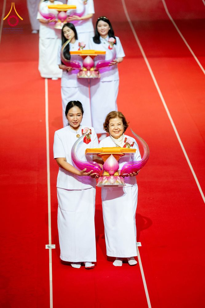 กลุ่มผู้หญิงสวมชุดขาวถือพานพุ่มอัญเชิญผ้าไตรเดินบนพรมสีแดง