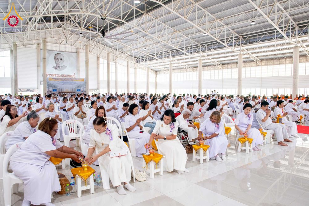 พุทธศาสนิกชนสวมชุดขาวนั่งพนมมือร่วมพิธีทางศาสนาภายในอาคารโถงกว้าง